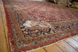 Vintage Mahal carpet corner showing navy border, dusty red field, and exposed foundation.