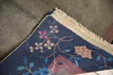 Peking carpet corner displaying delicate pink and beige blossoms, indigo pile, visible back and fringe.