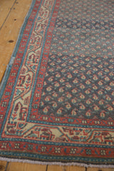 Angled close-up of the meandering vine border and boteh field of a distressed Serbend rug.