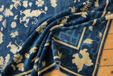 Antique Peking carpet fold revealing ivory butterfly, blossom, and infinity knot motifs on denim blue.
