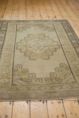 Distressed Oushak rug corner, showing geometric spandrel and banded border in beige and sage.
