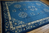 Close-up of a vintage Chinese Peking carpet corner with indigo border, ivory floral vines, and blue medallions.