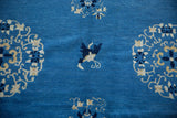Denim blue field of the vintage Chinese Peking rug with ivory floral patterns and a dark butterfly.