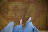 Top-down view of distressed Oushak rug, featuring worn gold and aubergine floral patterns.