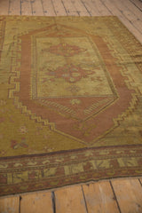 Distressed vintage Oushak carpet corner, showing faded stepped border and muted saffron yellow tones.