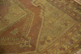 Close-up of distressed Oushak rug pile with dusty saffron and reddish-brown floral patterns.