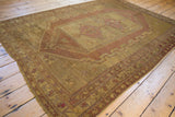 Distressed Oushak carpet corner with fringe, showing gold and mauve hues and visible wear.