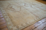 Distressed vintage Oushak rug with abrashed beige field and geometric starburst border.