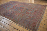 Distressed Belouch carpet with geometric patterns in terracotta, red, and blue tones.