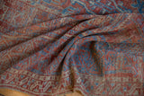 Distressed texture of the antique Belouch carpet, featuring geometric terracotta and indigo patterns.