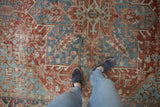 Vintage distressed Heriz rug showcasing worn pile and brick red, denim blue motifs.
