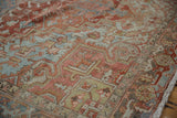 Distressed vintage Heriz rug showing geometric patterns in brick red, powder blue, and lime green with fringe.