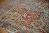 Distressed Heriz carpet with detailed geometric and stylized motifs in muted brick red, blue, and olive.