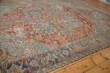 Distressed brick red and denim blue Heriz rug corner with visible foundation wear.