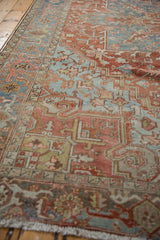 Distressed Heriz rug corner, brick red and denim blue, with stepped palmette motifs and aged patina.