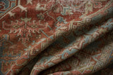 Textured close-up of vintage distressed Heriz rug with worn brick red and faded denim blue patterns.
