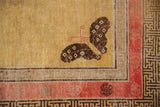 Antique Khotan rug corner with charcoal butterfly, pale raspberry inner border, and geometric T motif.