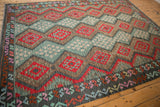 Afghani Kilim carpet detail of red geometric guls, aqua floral patterns, and multicolor cloudband borders.