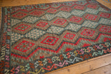 Vintage Afghani Kilim detail showcasing cherry red palmettes, zig-zag border, and floral motifs.