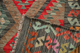 Folded Afghani Kilim rug detail, showing serrated geometric pattern, handwoven texture, and colorful stitched edge.