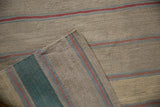 Folded Afghani Kilim rug corner reveals textured beige, pale blue, and dusty red stripes.