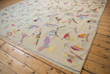 Angled view of a pictorial kilim with colorful stitched birds scattered across an ivory field.