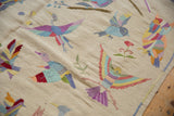 Angled view highlighting the raised stitching of colorful bird motifs on the ivory kilim weave.