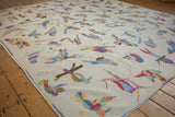 Wide angle view of a Pakistani kilim's ivory field, filled with colorful, textured bird motifs.