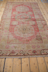 Pale dusty cherry red Khotan rug with floral roundel medallion, beige palmettes, and wave border.