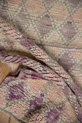 Close-up of distressed Moroccan rug pile, showing varied purple, rose, and ivory textures.