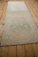 Distressed vintage Oushak runner's soft ivory pile and faded pale green trellis pattern.
