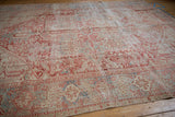 Textured close-up of a distressed Karaja carpet showing faded cherry red, pale blue, and ivory patterns.