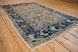 Distressed Bijar rug corner with navy blue arabesque border and worn beige pile.