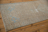 Vintage distressed Borchalou rug's beige field, blue medallion, germinating blossoms, and serrated border.
