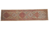 Vintage distressed Serab rug runner with a column of geometric medallions in pale red and blue over a beige field.