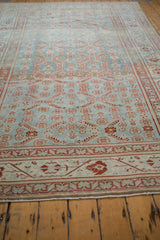 Angled view of a distressed Malayer carpet's repeating red floral motifs on an abrashed powder blue field.