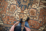 Antique Serapi carpet with intricate terracotta, navy, and ivory geometric botanical patterns.