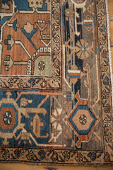 Terracotta, navy, and beige stylized serrated leaves on an antique Serapi rug corner, with fringe.