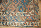 Antique Kurdish rug corner: geometric lattice field, meandering vine border, and visible pile wear.