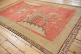 Coral field of the antique Khotan rug, with asymmetric pictorial blossoms and ivory border.