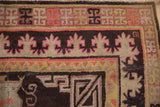 Khotan carpet corner, displaying geometric borders and stylized motifs in chocolate, ivory, and vivid pink.