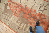 Vintage Khotan carpet section showing deer and snowflake tree design on terracotta ground with wear.