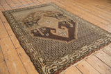 Distressed vintage Hamadan rug corner: coffee brown and ivory geometric border, abrashed field, subtle motifs.
