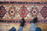 Hand-knotted West Persian runner detail: ivory ground, geometric red and royal blue medallions.