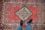Vintage Arak rug with diamond medallion, floral border, abrashed brick red field and wear, under boots.