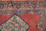 Detail of vintage Sarouk rug: ornate floral medallion, meandering border, brick red field, visible wear.