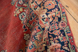 Vintage Arak rug showing abrashed brick red field, navy blue floral border, and visible foundation wear.
