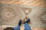 Feet standing on a distressed Oushak runner, showing faded ivory and brown starburst designs.