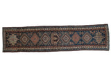 Vintage Karaja Persian runner with a column of geometric medallions in rust, terracotta, and teal on a navy field.