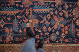 Antique Persian Heriz carpet close-up, primitive floral and bird motifs in navy blue and brick red.